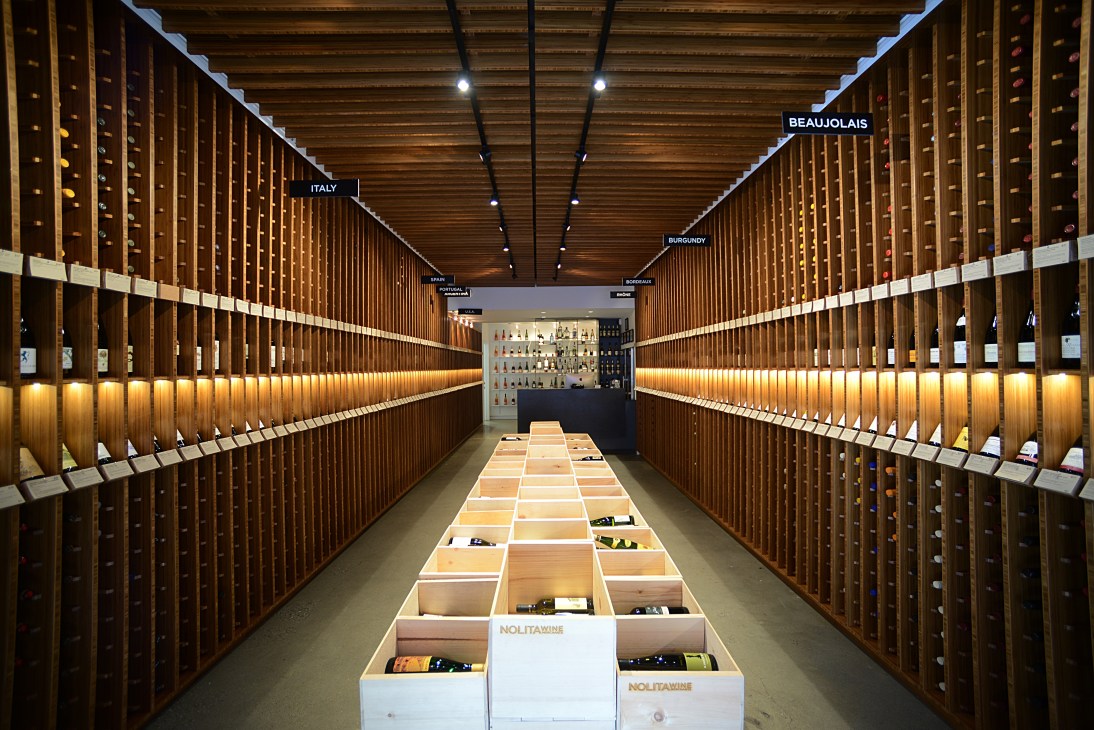 Interior of NoLita Wine Merchants with wooden wine storage racks on either side and illuminated central display, New York.