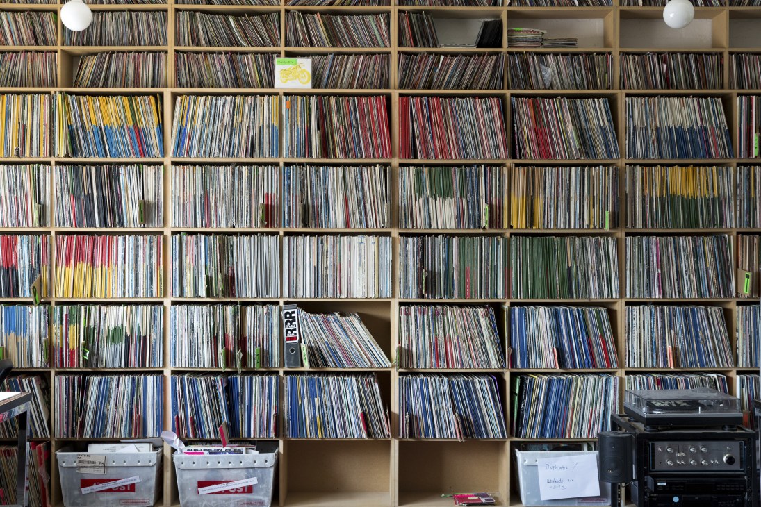 Extensive wooden shelving unit filled with organized vinyl records and CDs at Triple R radio station.