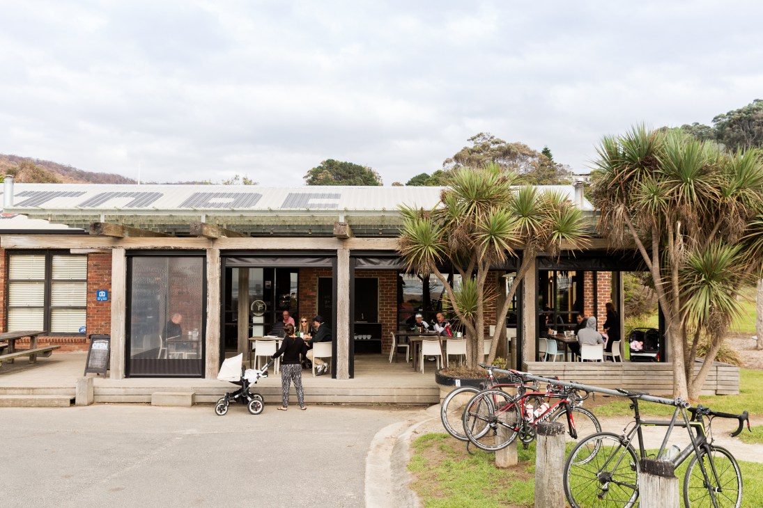 Wye River General Store entrance with brick facade, large windows, and customers dining outdoors under palm trees.