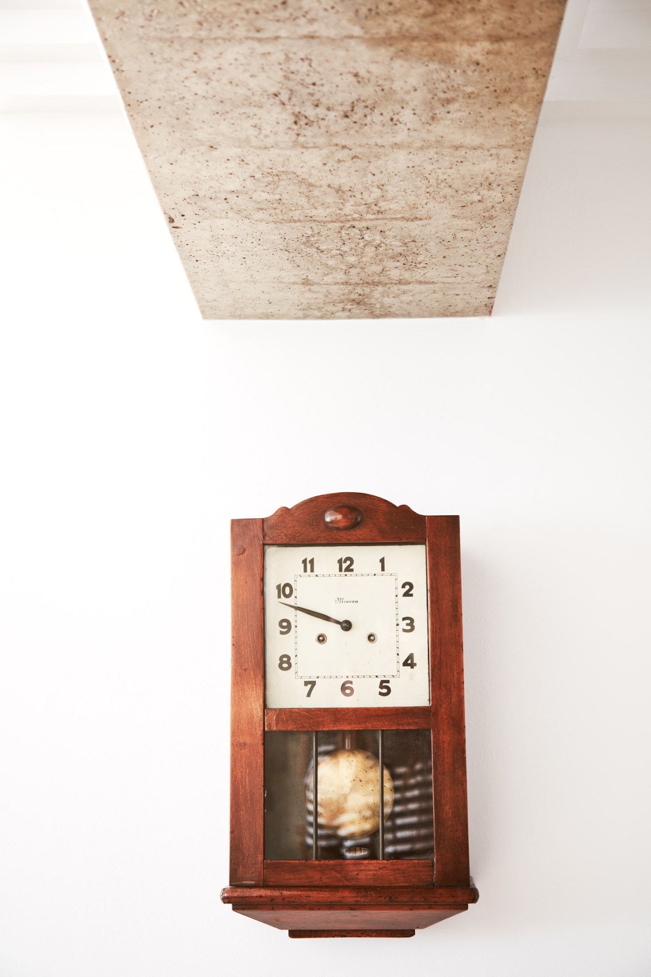 Vintage wooden pendulum wall clock with cream face and dark wood case against white background.