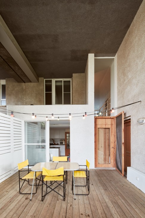 A modern brutalist terrace with yellow chairs around a wooden table, overlooking an interior courtyard of Espai Verd apartment building.