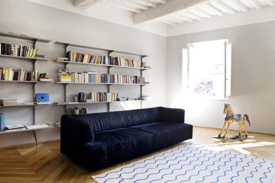 Modern living room with dark blue sofa, built-in shelving, exposed ceiling beams, and geometric patterned rug.