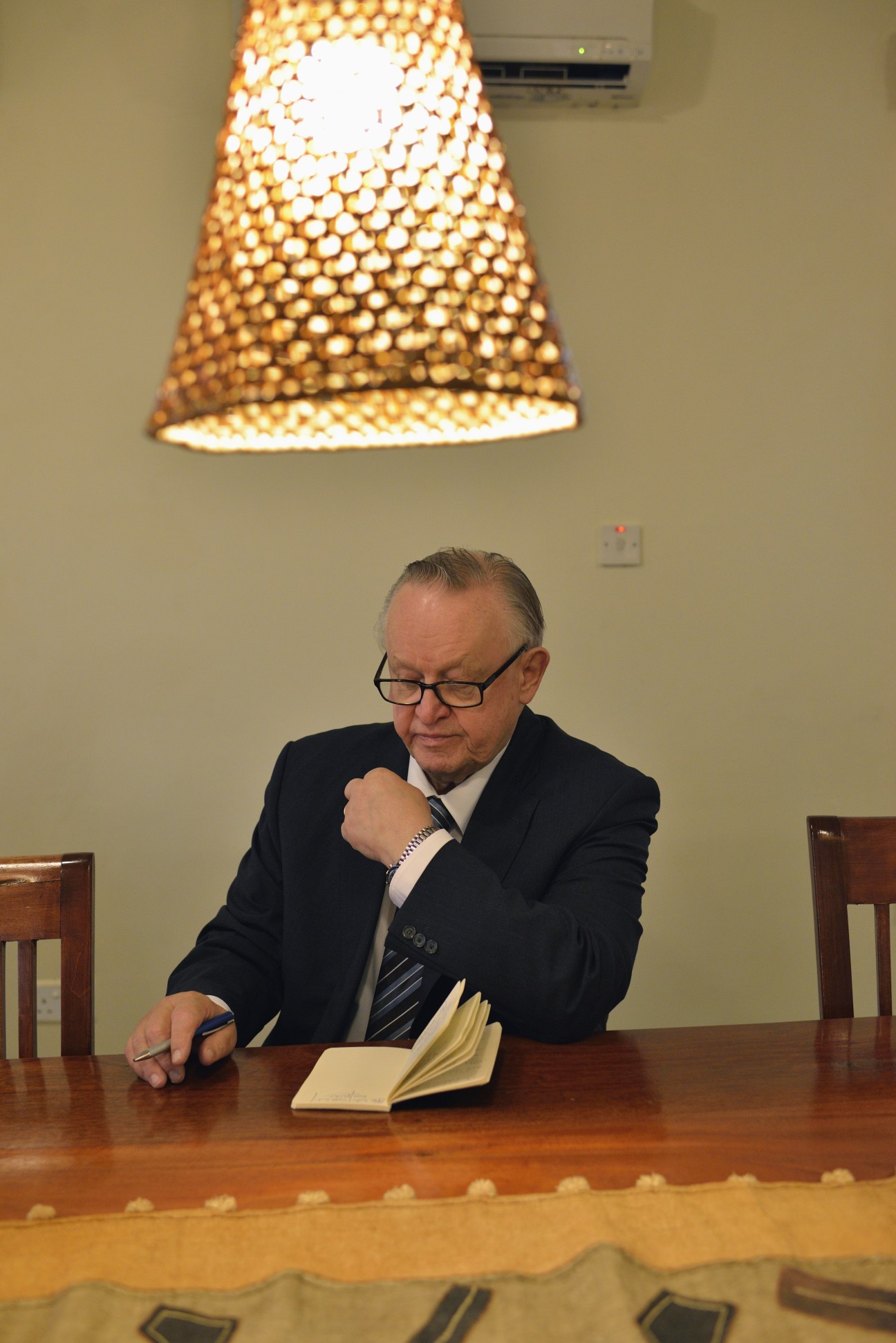 Finnish ex-president Martti Ahtisaari sits at a wooden table reviewing documents under a pendant lamp.