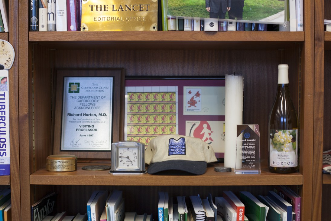 Wooden shelf displaying awards, a clock, wine bottle, and medical publications including Richard Horton's credentials.