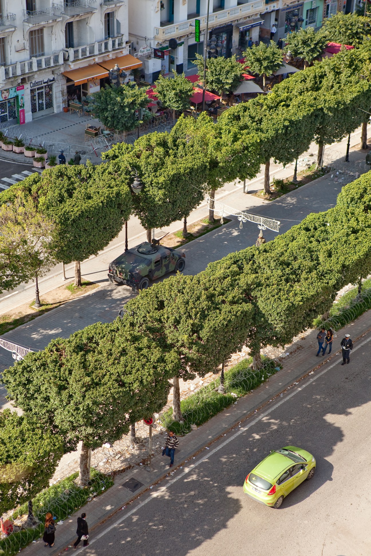 Aerial view of Avenue Bourguiba in Tunis showing tree-lined street with cafés, shops, and military vehicle
