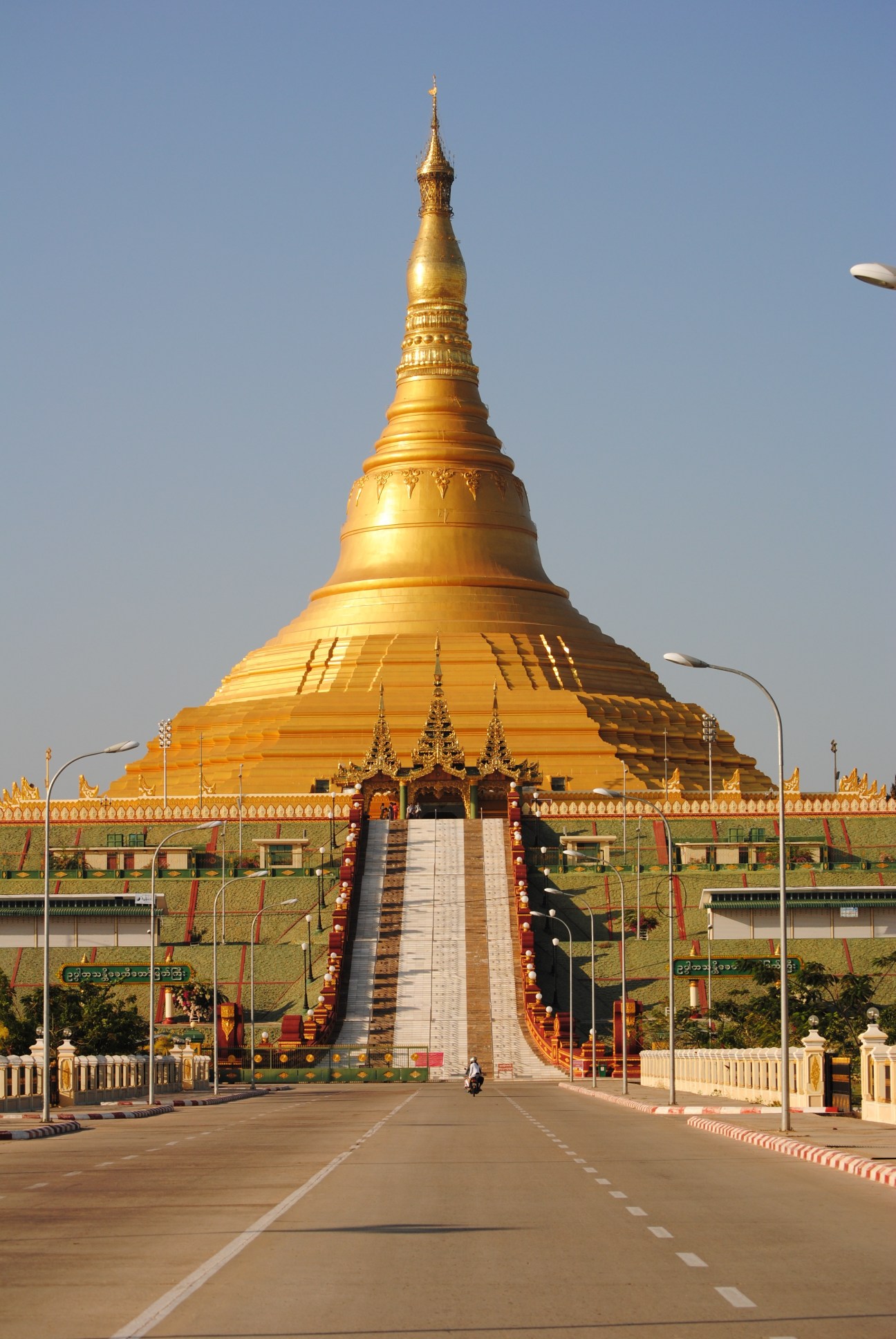 Golden Uppatasanti pagoda in Naypyidaw with wide empty road and modern street lamps.