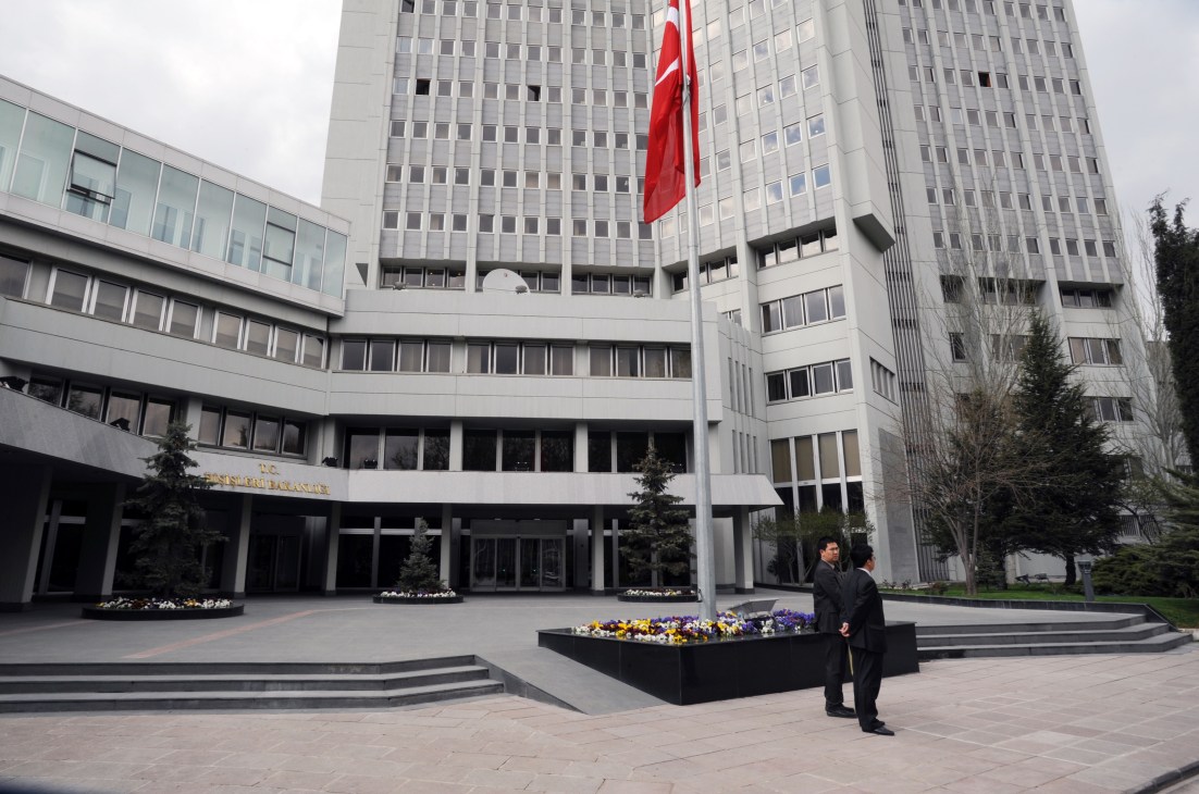 The Ministry of Foreign Affairs building in Ankara with Turkish flag and two officials in the courtyard.