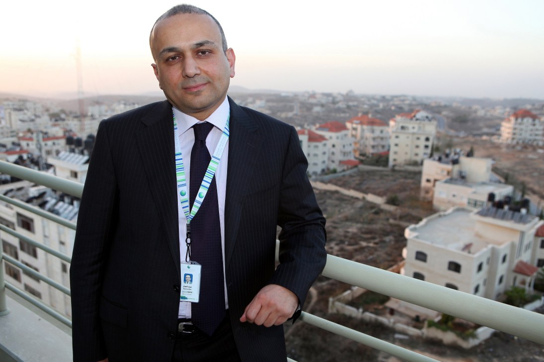 Ammar Aker, CEO of Paltel Group, stands on a high-rise balcony overlooking Ramallah's urban sprawl.