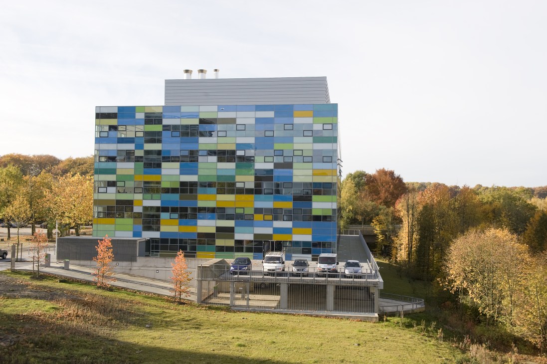 Modern building with colorful pixelated facade in blue, green, and yellow panels surrounded by autumn trees.