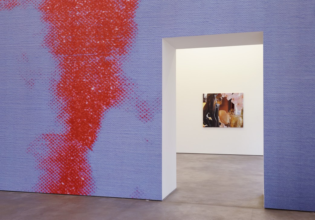 Louise Lawler's exhibition 'Taking Place' showing a small photograph on a gallery wall with red pixelated artwork visible on the left.