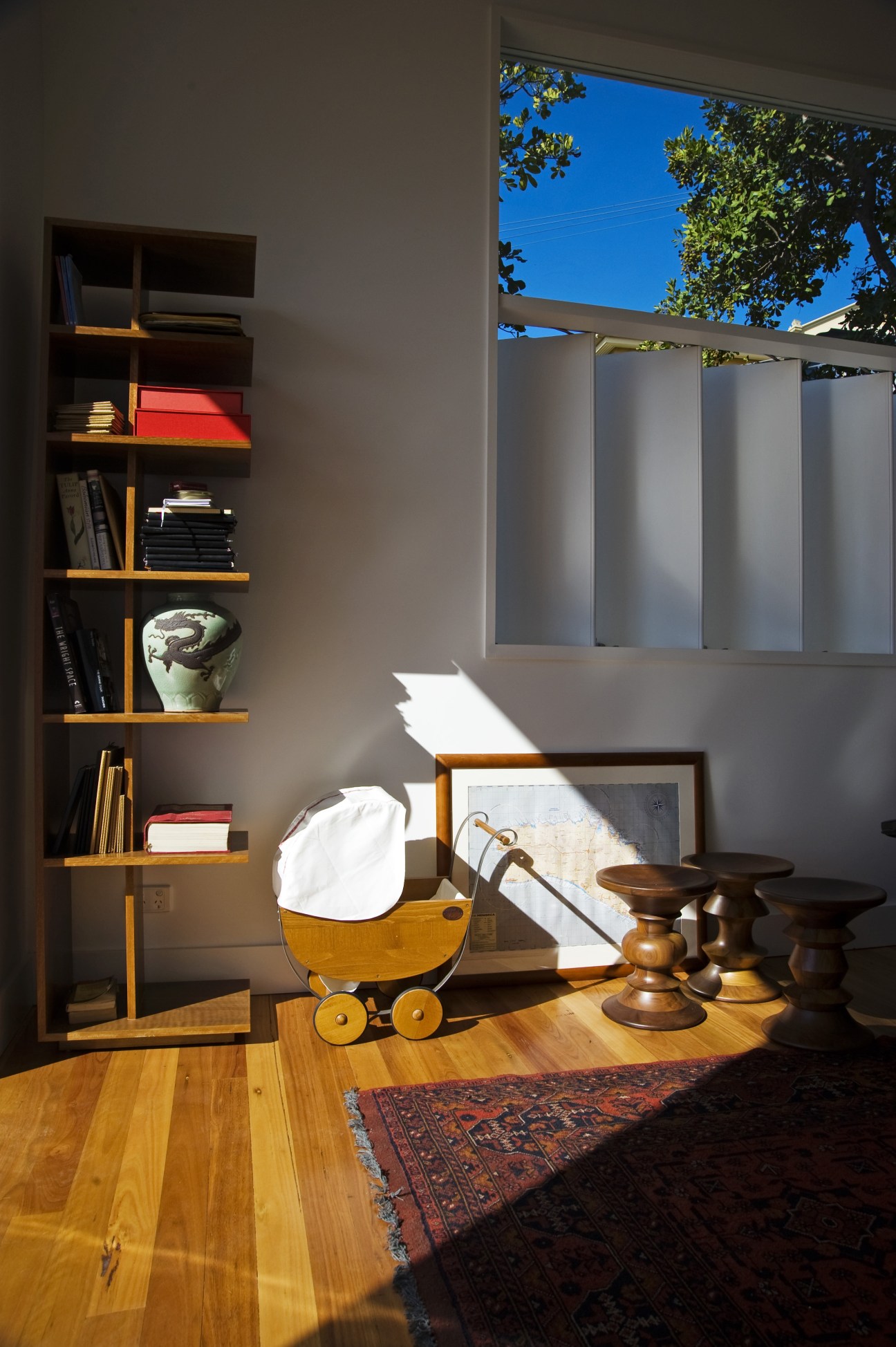 Sunlit interior with wooden shelving unit, wooden toy pram, and warm timber floors.
