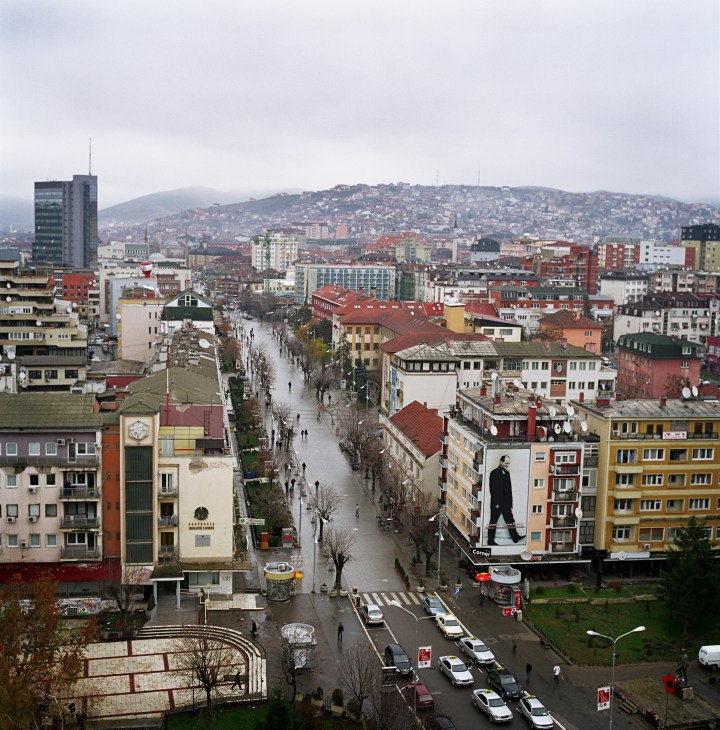 Aerial view of Pristina's city center with a large poster of Ibrahim Rugova on a building facade.