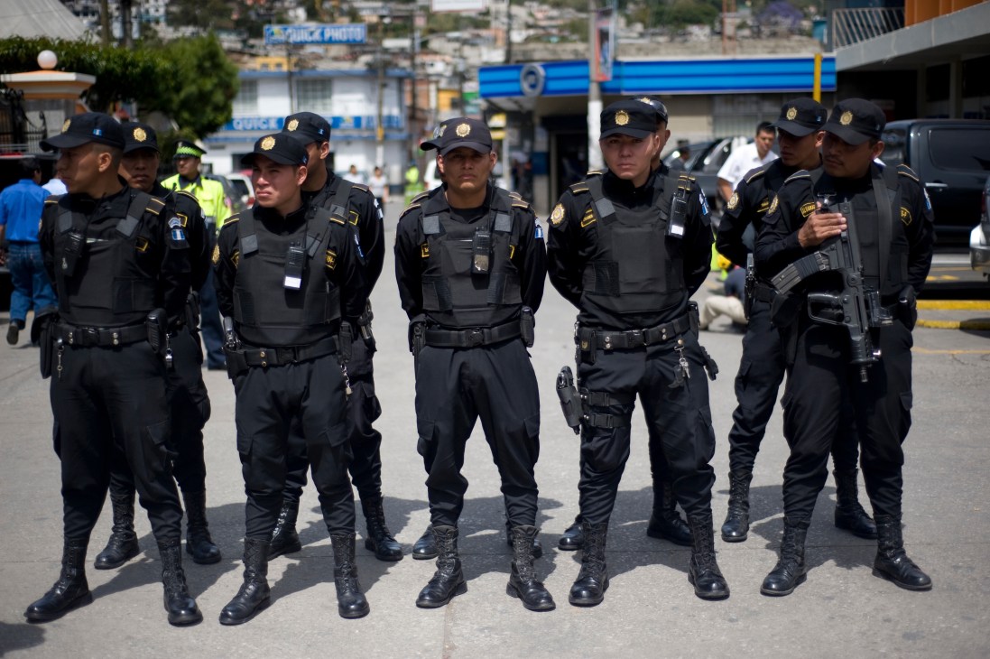 A line of armed Guatemalan police officers in black uniforms and caps standing on a city street.