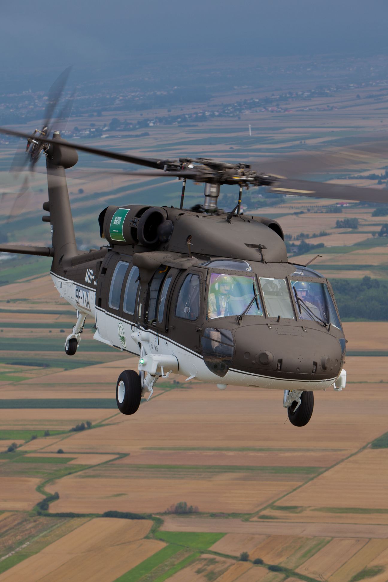 Sikorsky S-70i Black Hawk helicopter in flight over agricultural landscape.