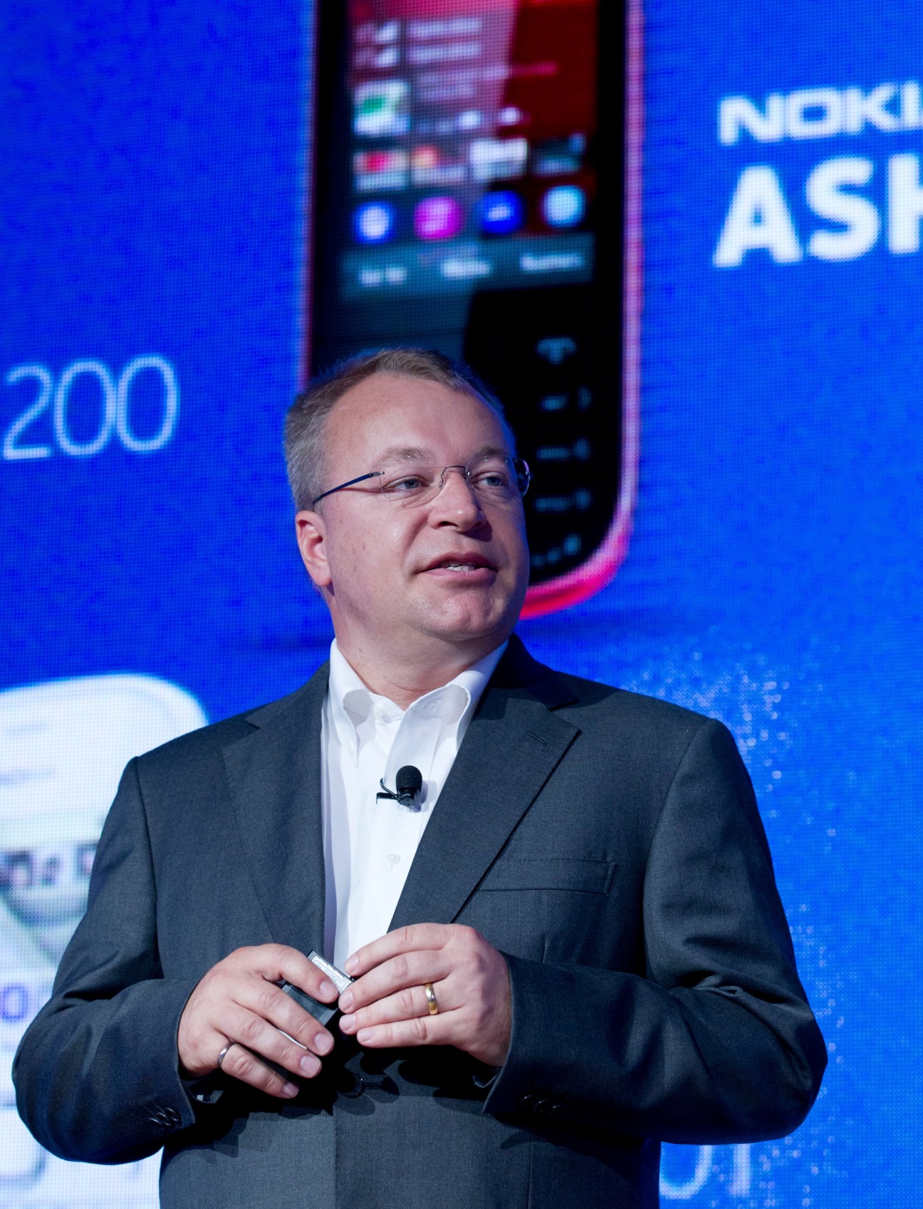 Nokia chief executive Stephen Elop speaking at a presentation with Nokia branding and a Lumia 920T smartphone displayed behind him.