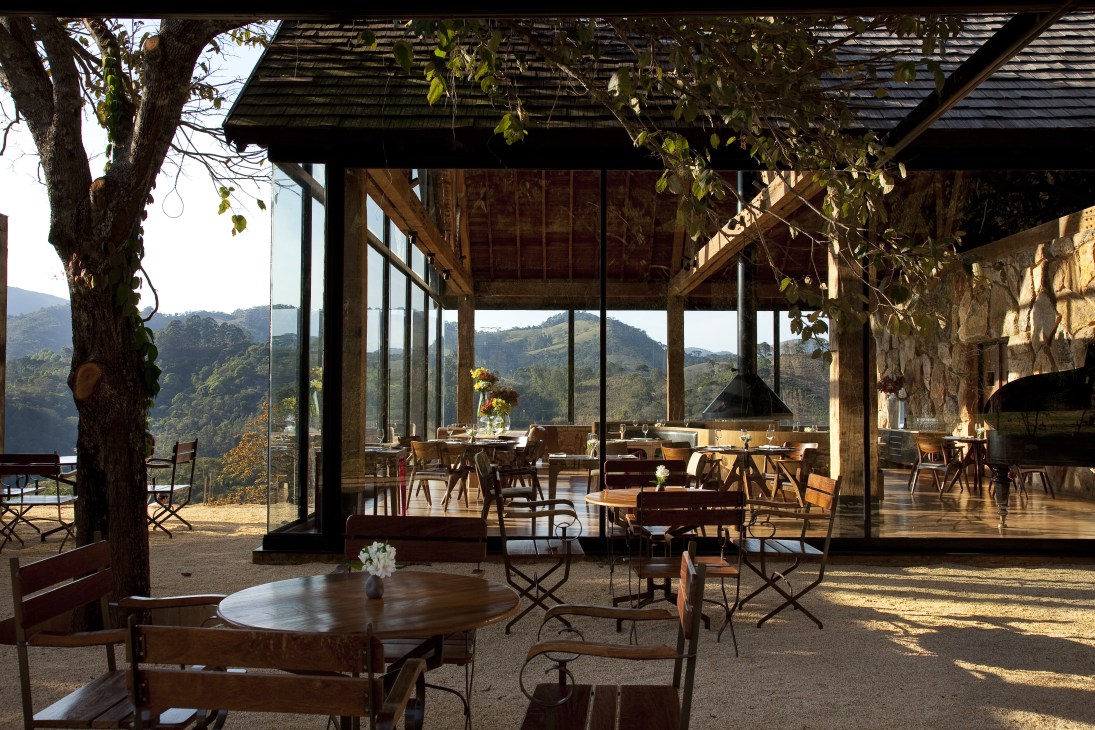 Interior of Botanique Hotel with wooden beams, large windows overlooking rainforest mountains, and modern furnishings.