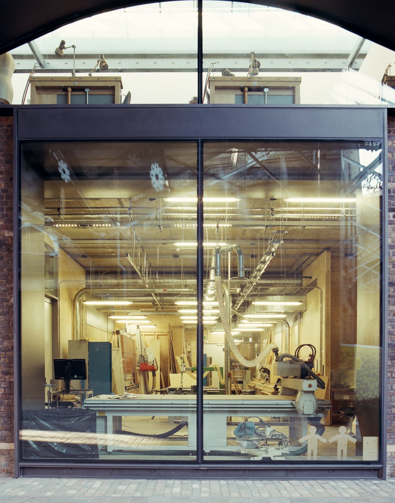 A workshop interior visible through large glass windows displaying woodworking tools and equipment.