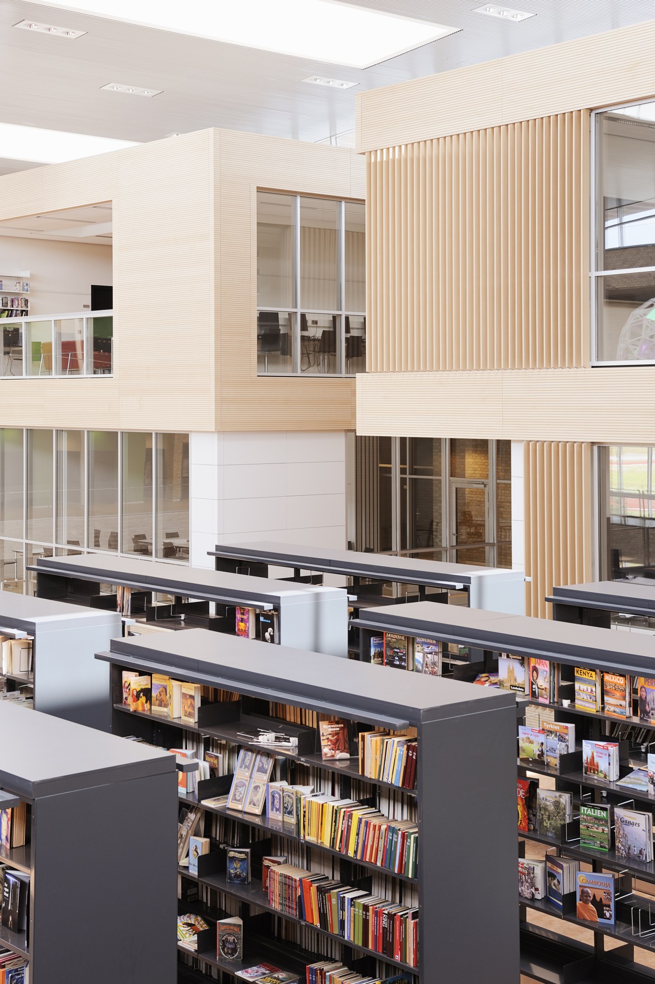 Open-plan library with black shelving units displaying books, wood-paneled walls, and glass-walled classrooms above.