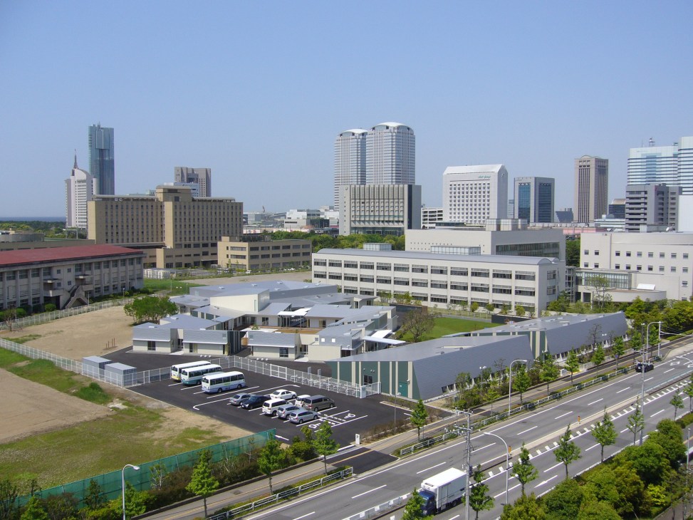 Aerial view of International school in Makuhari, Japan with low-lying buildings and surrounding cityscape.