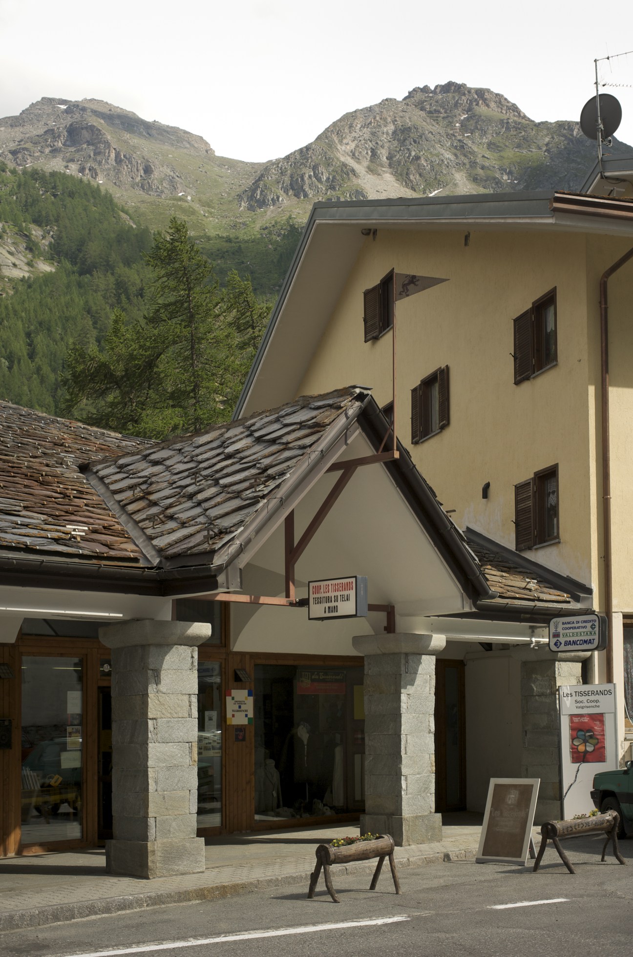 Les Tisserands Cooperative building nestled in Alpine valley with mountains in background.