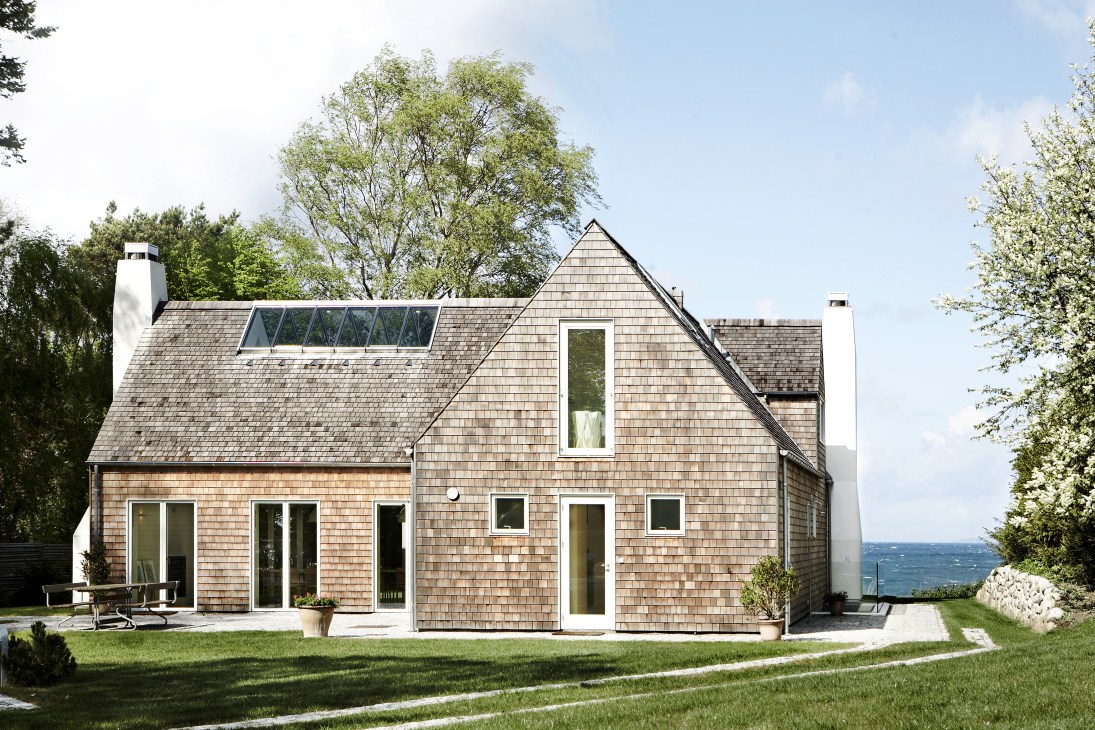 Modern wooden-shingled house with pitched roof overlooking the sea in Munkerup, Denmark.