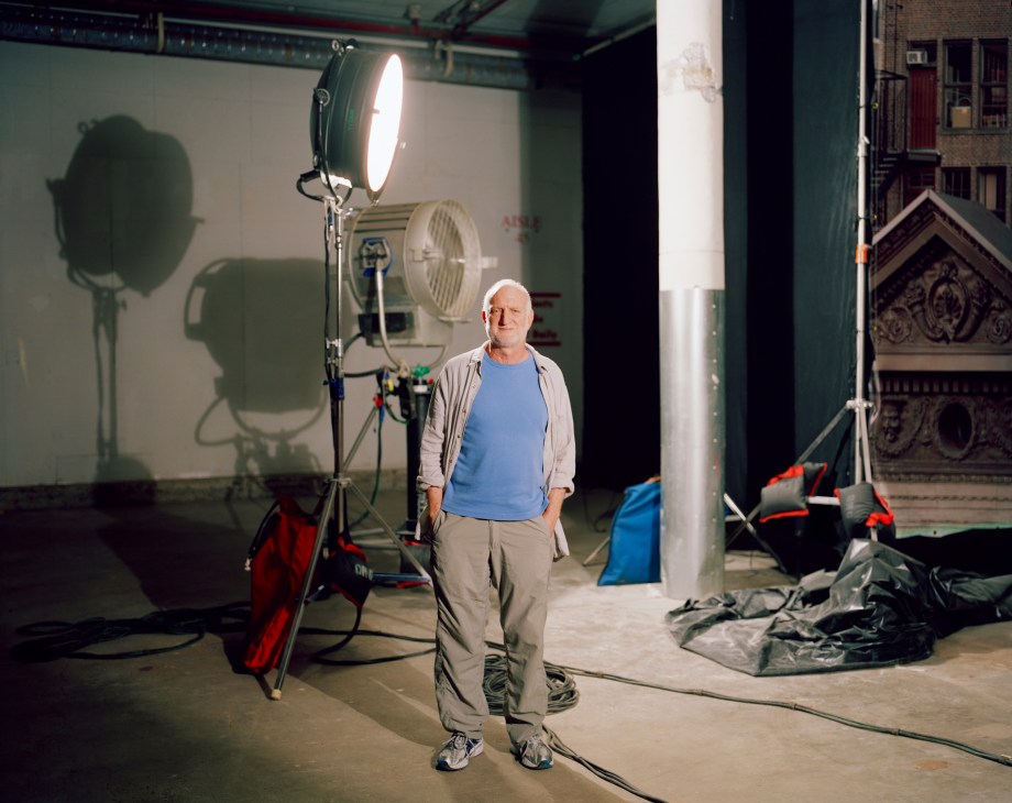 Dead of Night producer Gil Adler stands on a film set surrounded by professional lighting equipment and ornate architectural details visible in the background.