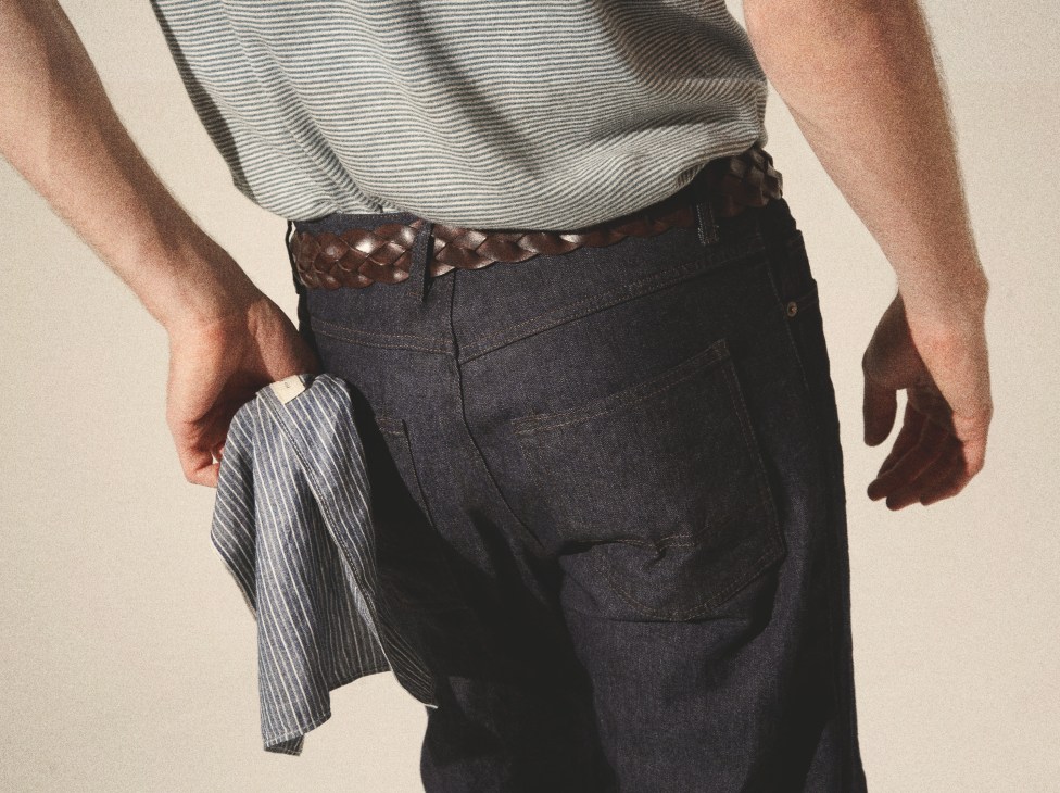 Man wearing striped shirt and dark jeans with brown woven belt and striped handkerchief.