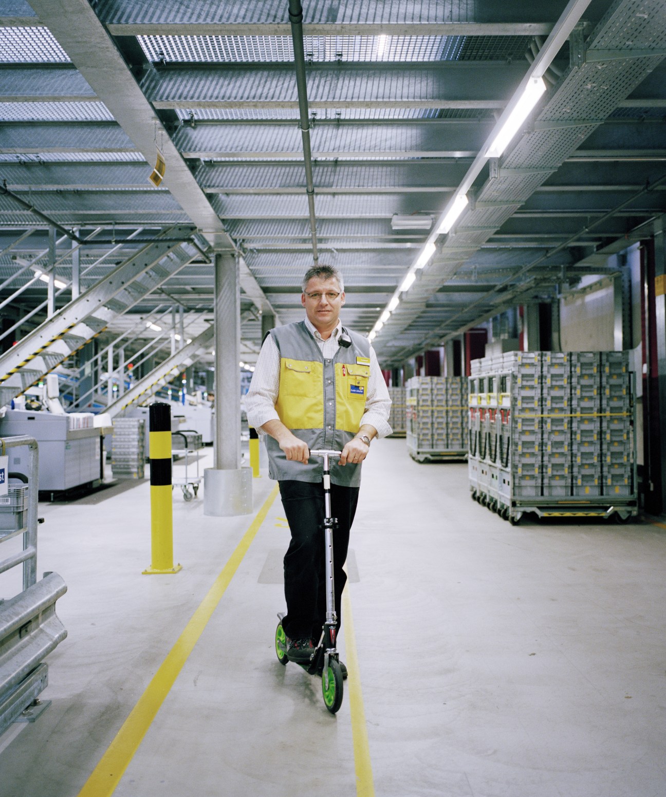 Guido Lötscher, shift supervisor at Härkingen sorting office, standing on a scooter in a modern postal facility.