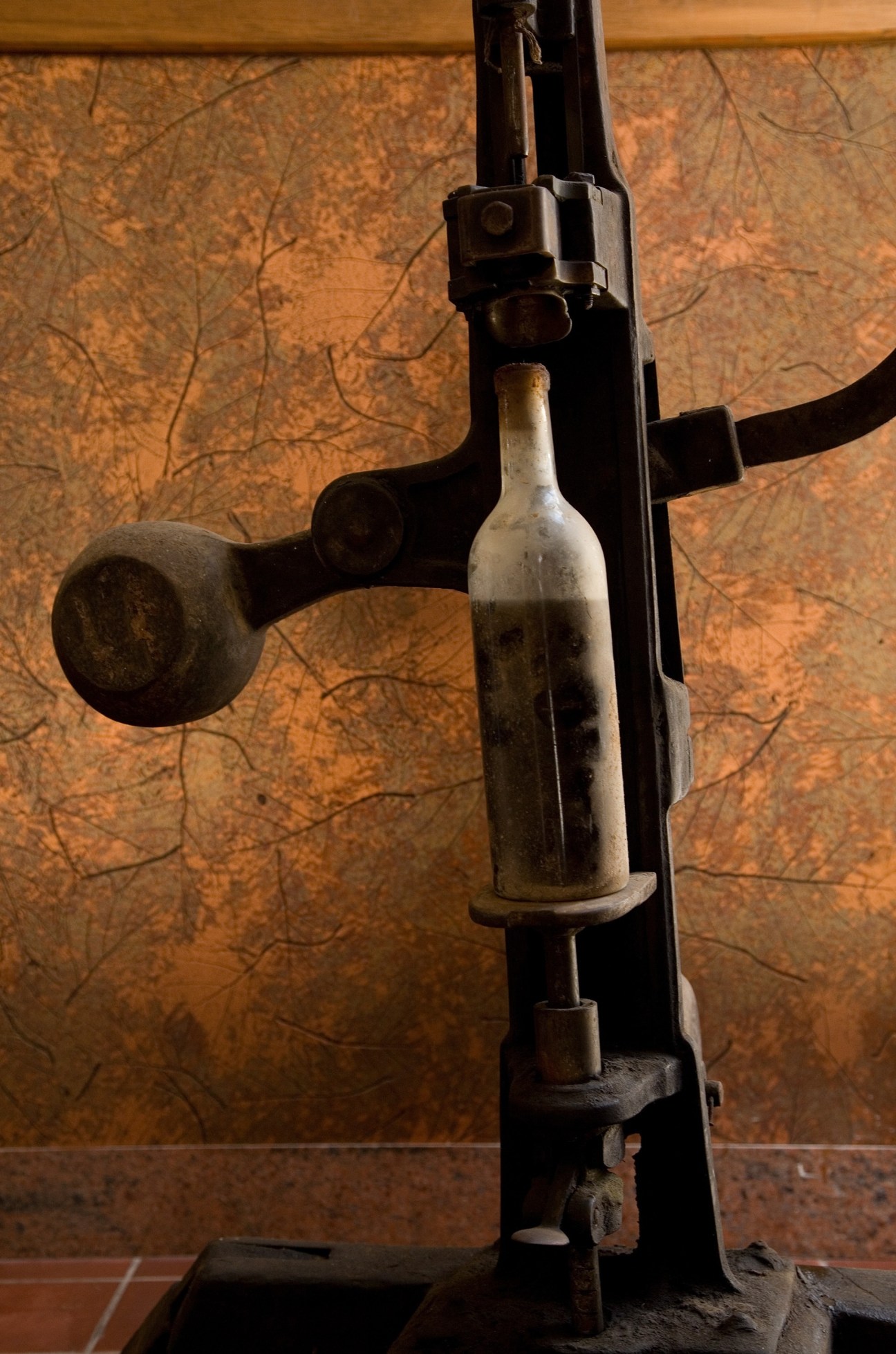 Vintage wine bottle held in an old black metal bottling machine against a textured brown background.