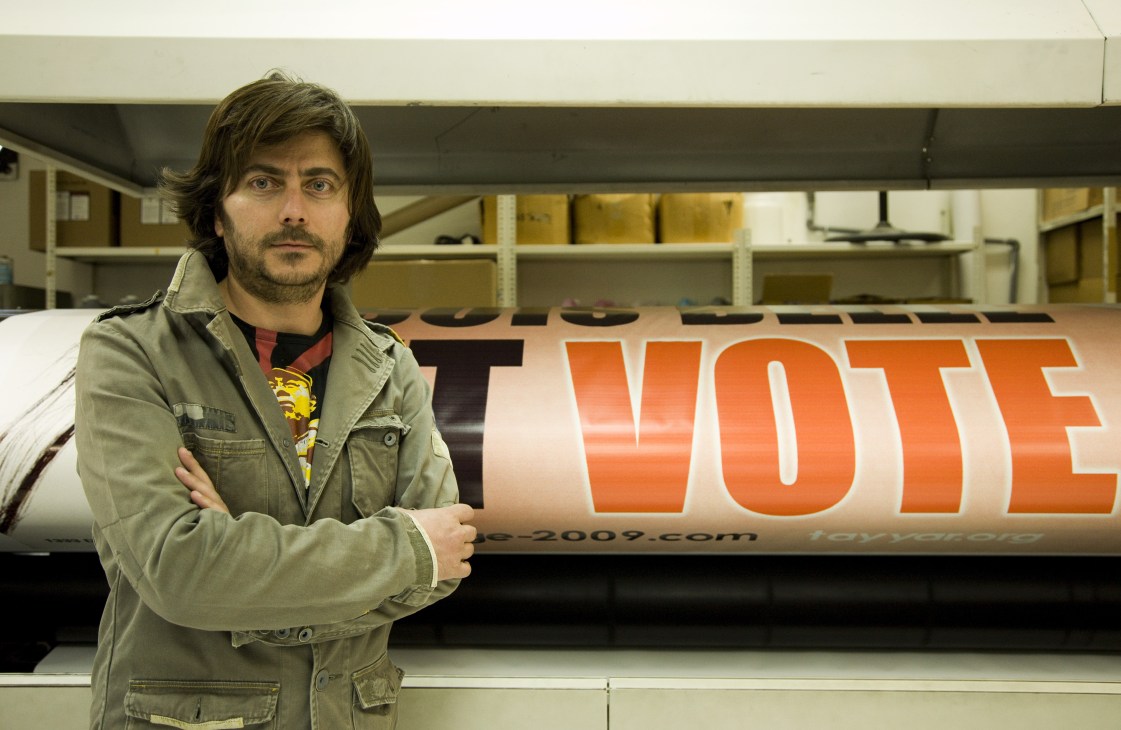 Sami Saab, creative director for Michel Aoun's Free Patriotic Movement, stands before an orange election poster he designed.