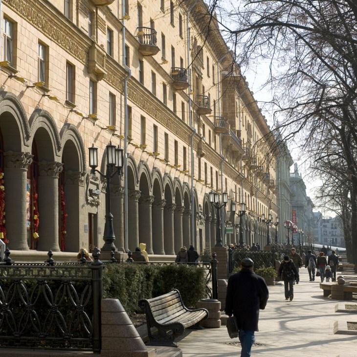 Stalinist-style colonnaded buildings line a wide pedestrian street in central Minsk with sparse foot traffic.
