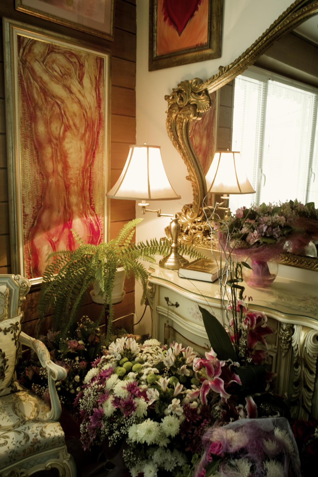 Ornate dressing table with bouquets of fresh flowers, lamps, and framed artwork in a luxurious Sofia apartment.