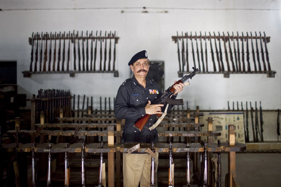 Waseem Ahmed, Karachi's police chief, holds a rifle in the armoury surrounded by stored weapons.