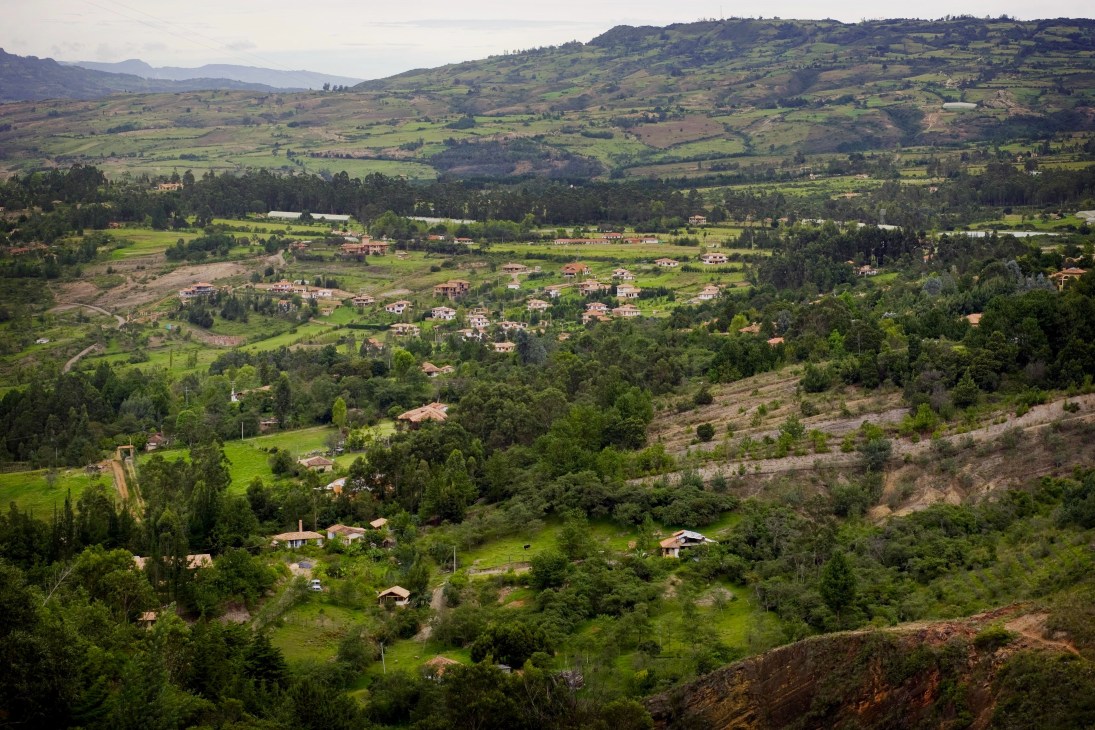 Aerial view of Villa de Leyva's rolling green countryside with scattered houses and mountains in the distance.