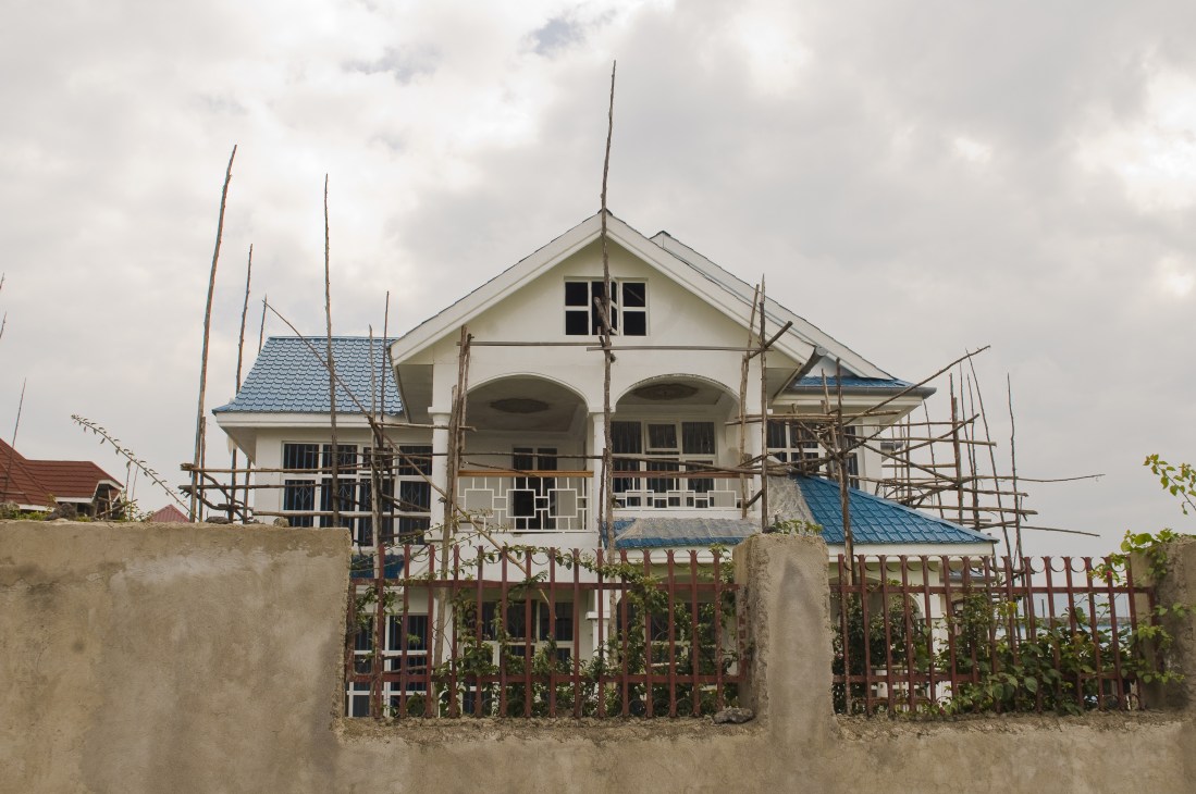 A two-story residential house under construction on Lake Kivu's shore with scaffolding and blue metal roofing.
