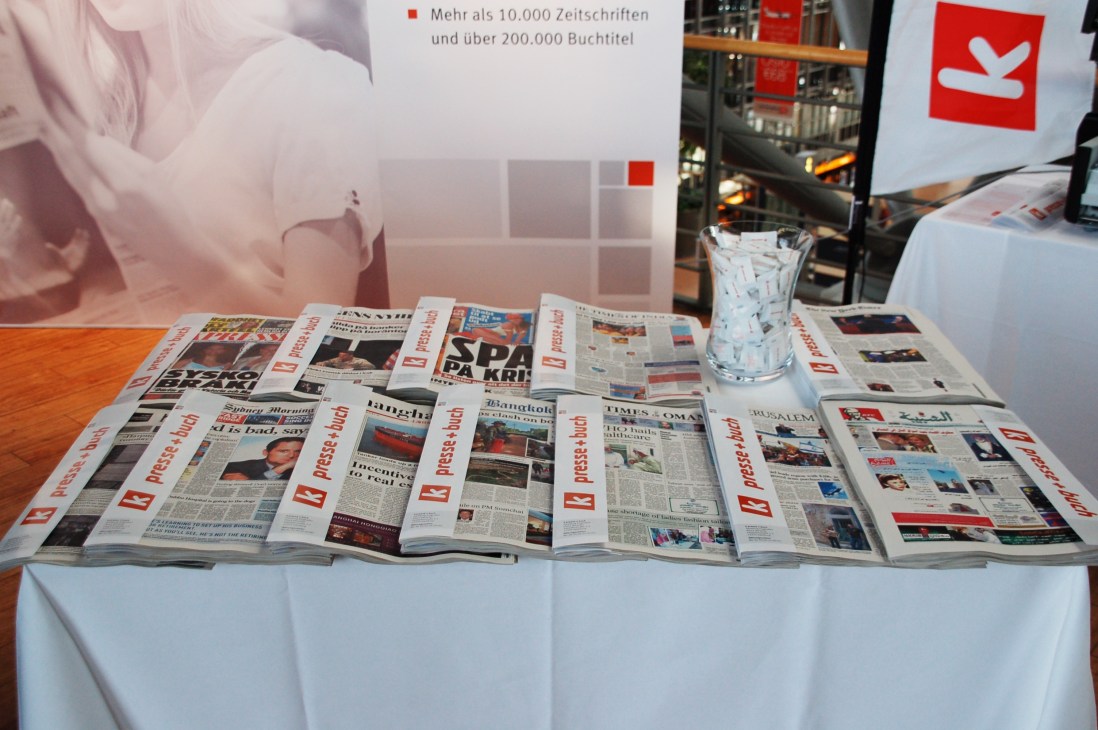 Multiple newspapers and magazines displayed on a white-clothed table at K Presse + Buch bookshop in Hamburg airport.