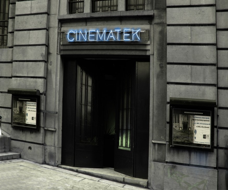 Cinematek's entrance with blue neon sign on concrete facade and black doorway.