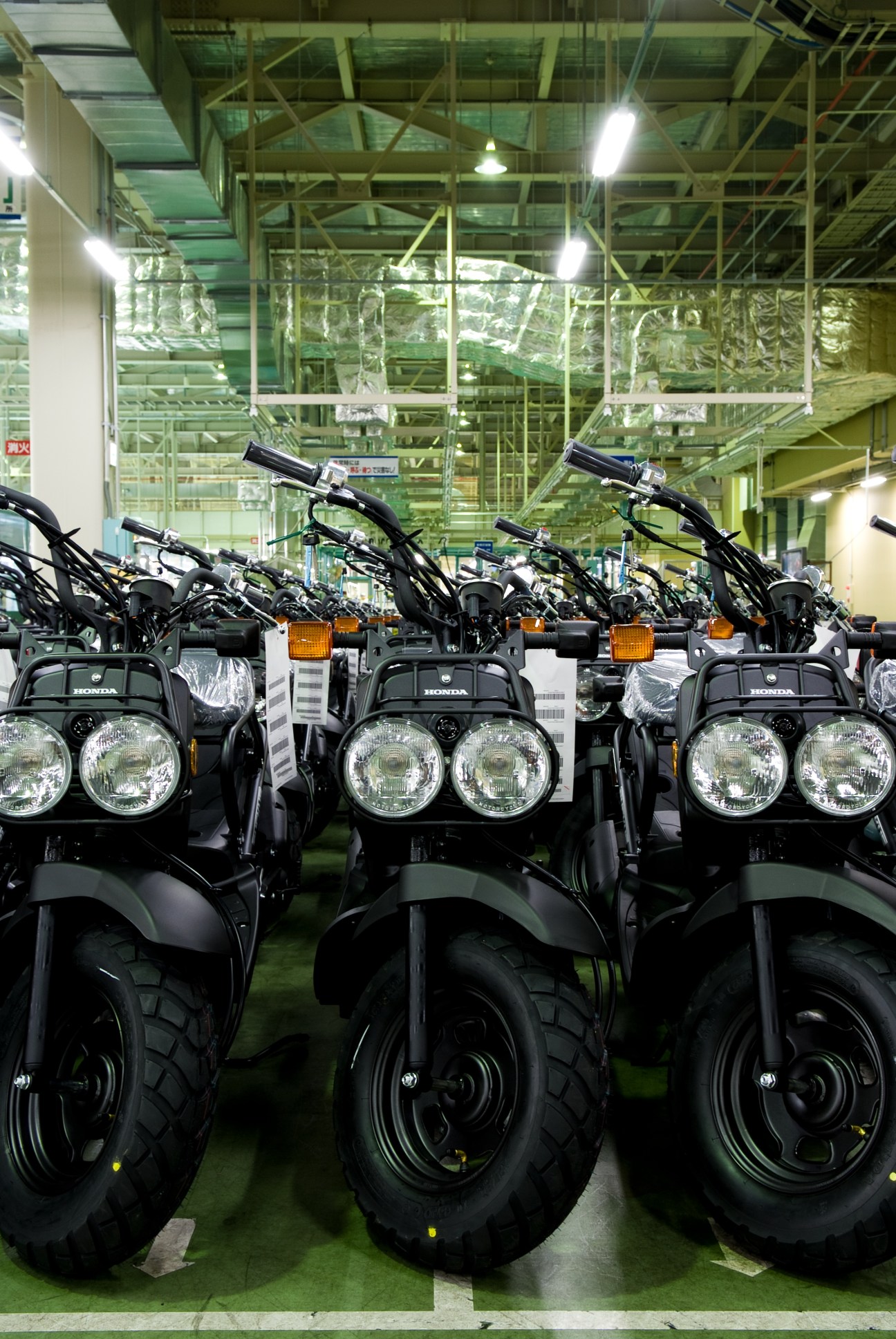 Three black Honda Zoomer scooters lined up in a factory with distinctive dual round headlights.