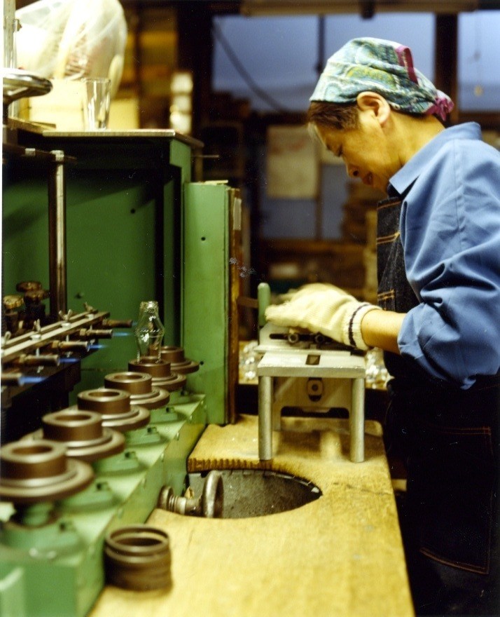 Craftsman smoothing hand-blown glass at Shotoku factory workstation.