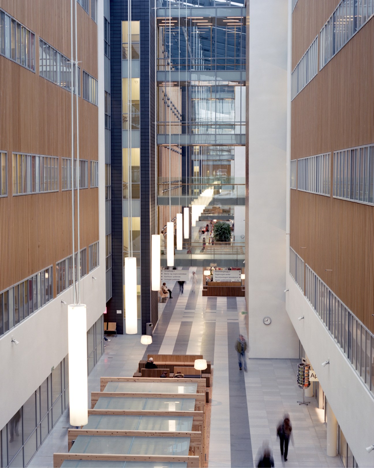 Wood-clad public atrium with cylindrical hanging lights designed by CF Møller at Akershus University Hospital.