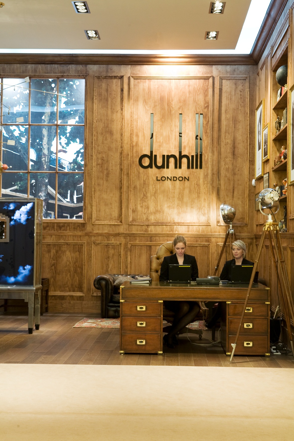 Dunhill London booth with wood-panelled walls, desk, and staff at Geneva watch fair.