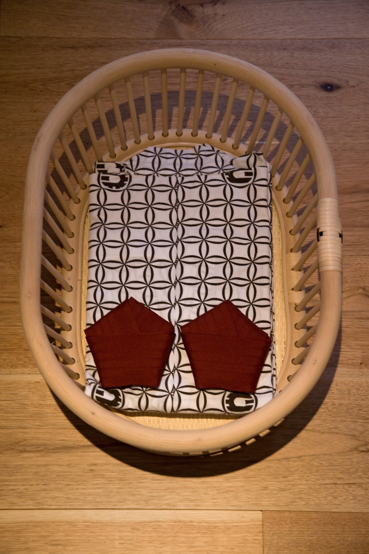 Wooden basket with geometric patterned fabric and red cushions on wooden floor.