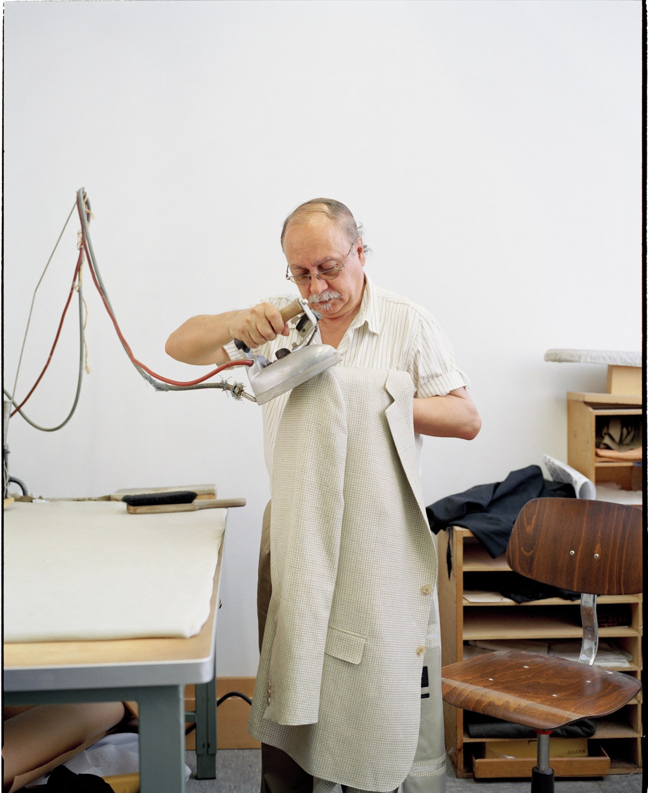 Man in light-colored shirt using pressing equipment on a suit at Regent tailoring workshop.