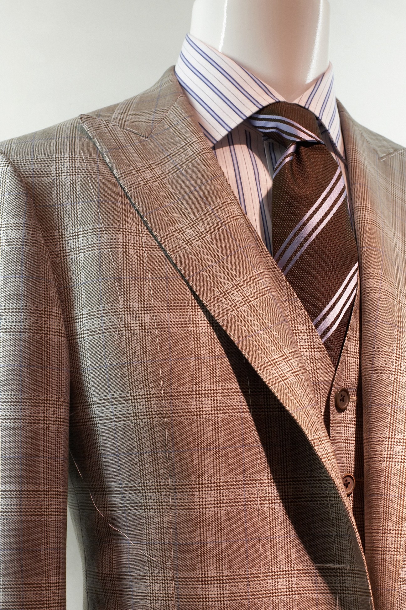 Pared down suit by Corneliani in beige plaid with striped shirt and tie on mannequin.