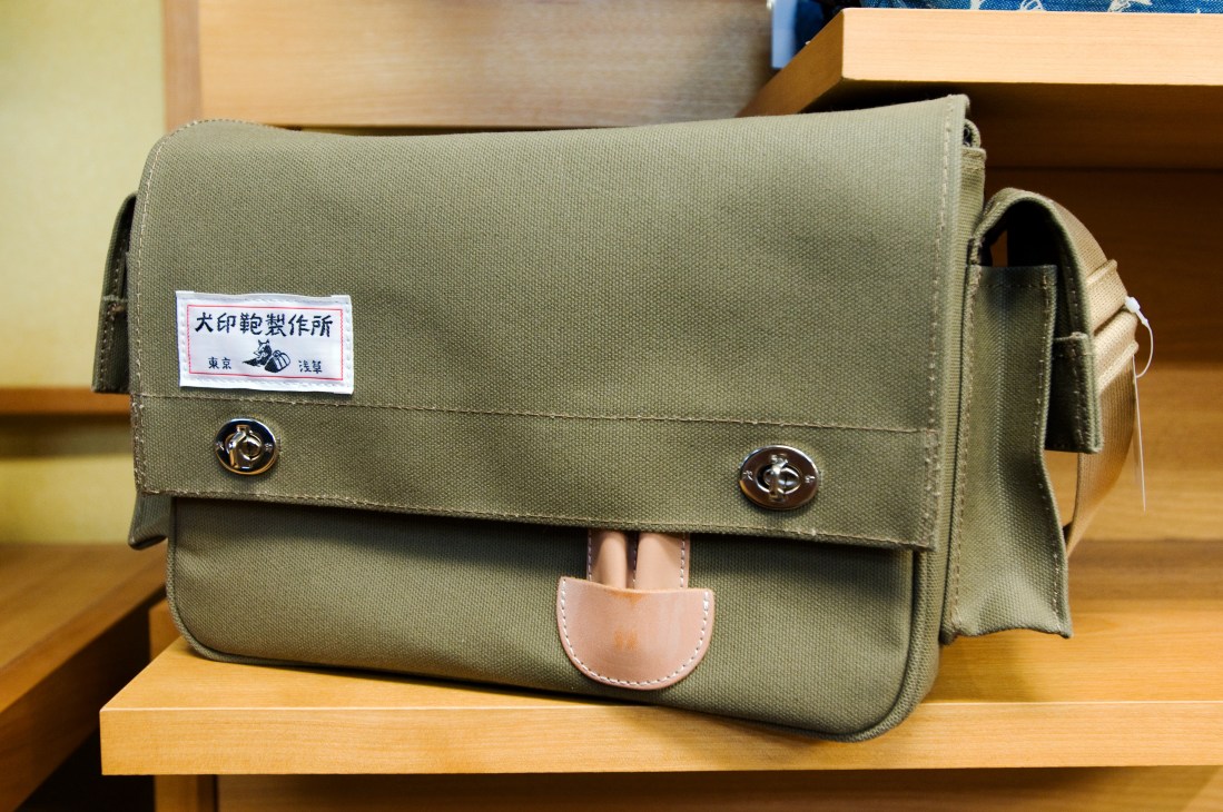 Inujirushi shoulder bag in sage green canvas with leather trim and metal dog logo buttons.