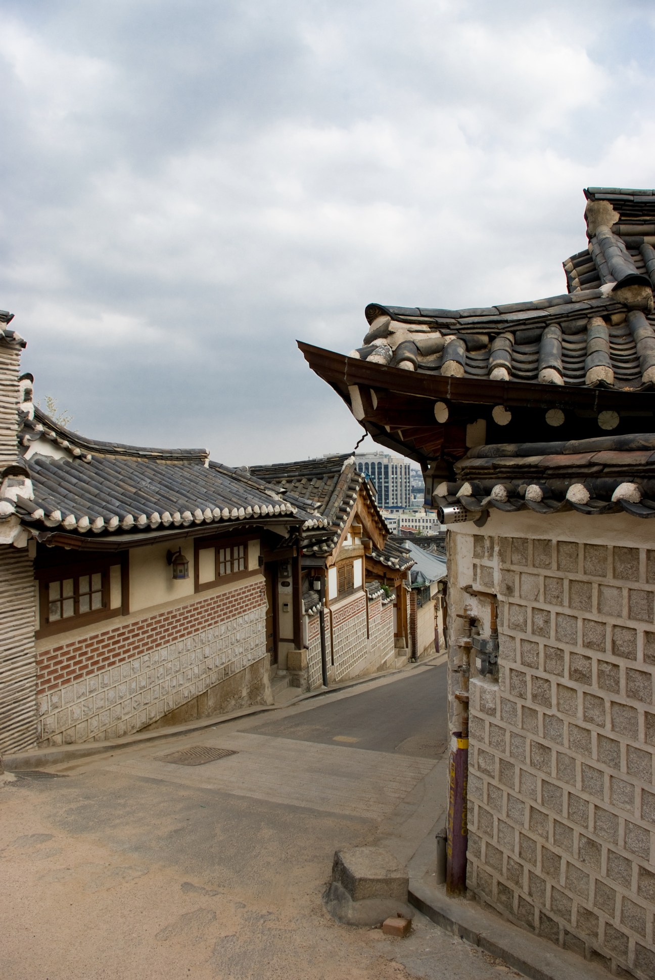 Traditional hanok houses with curved tile roofs in the Bukchon neighborhood of Seoul, with modern high-rise buildings visible in the background.
