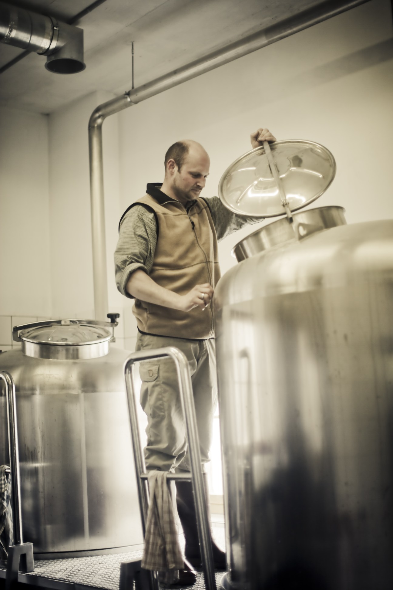 Master brewer Florian Geyer working with large stainless steel fermentation vats in a brewery.