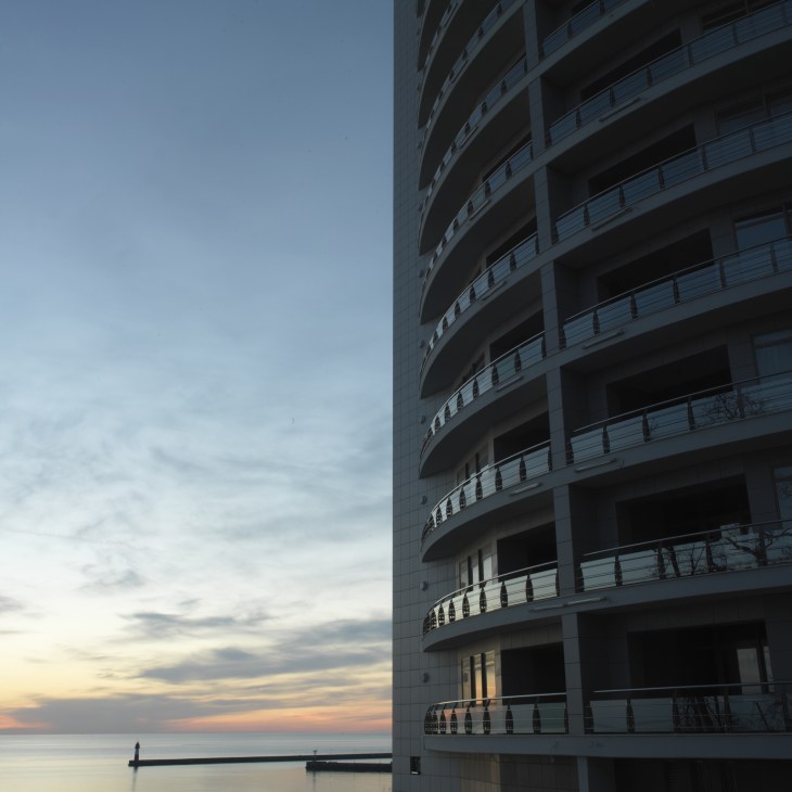 Curved modern residential building with multiple balconies overlooking the Black Sea at sunset.