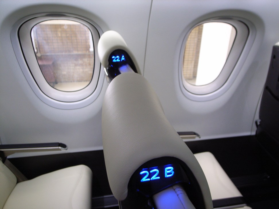 Interior view of Mitsubishi Regional Jet cabin showing white seat with blue digital display and windows.