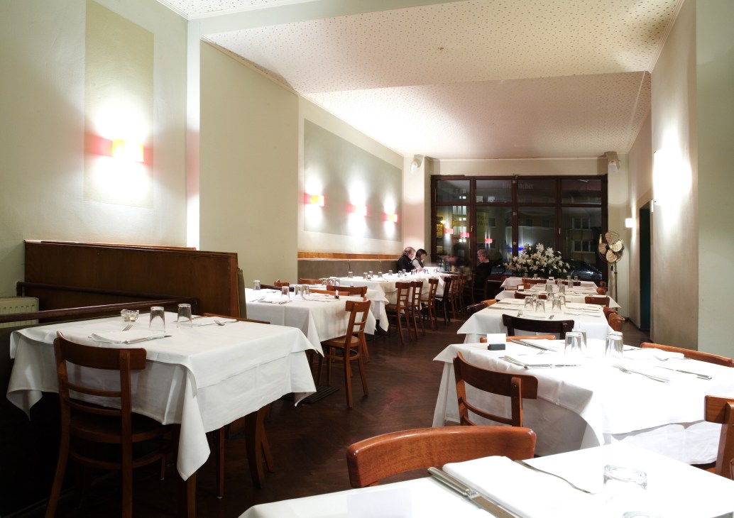 Minimalist dining room at Cantamaggio with white tablecloths, wooden chairs, and soft lighting.
